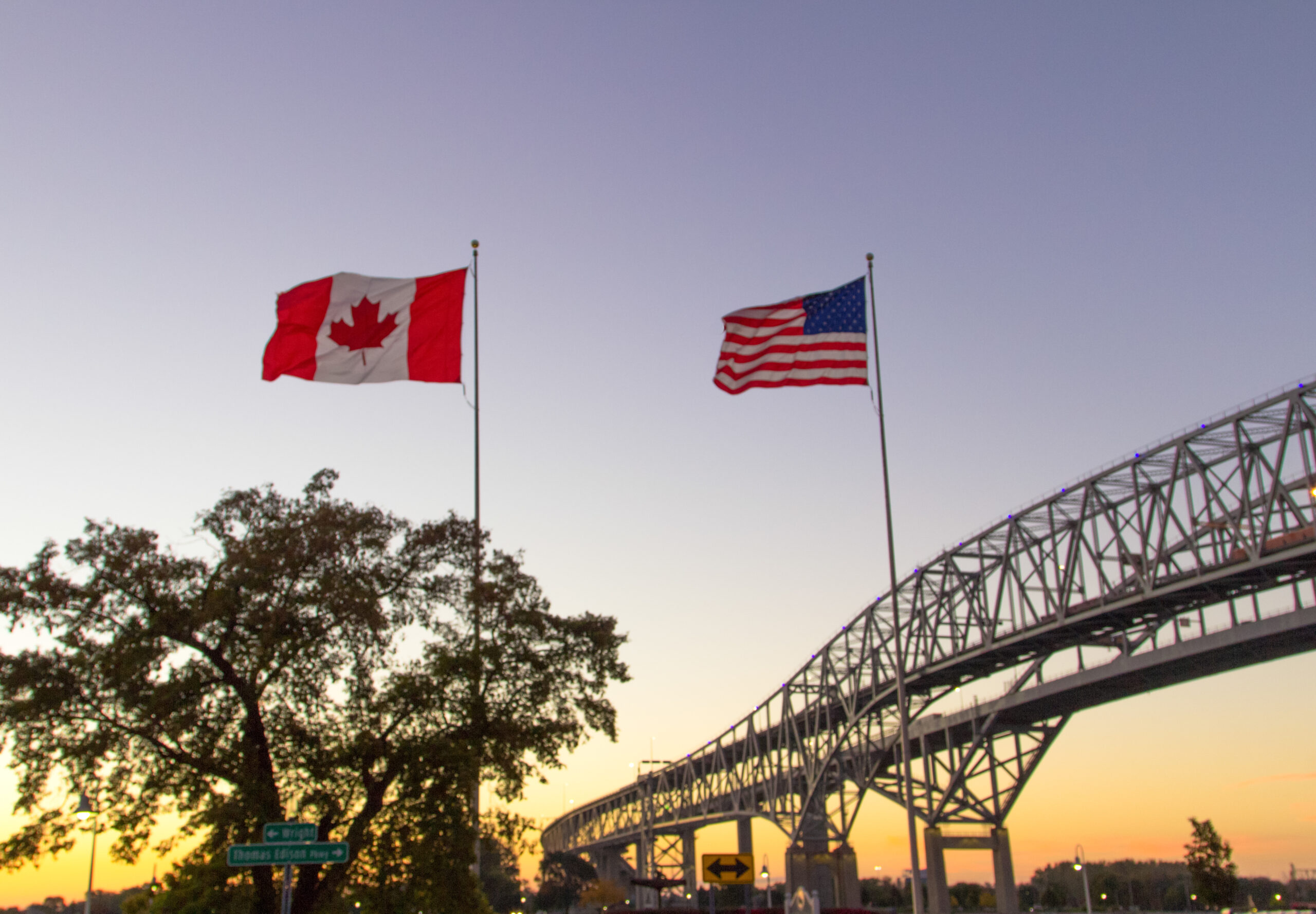 An picture of Canadian and American flags with a bridge in the background.